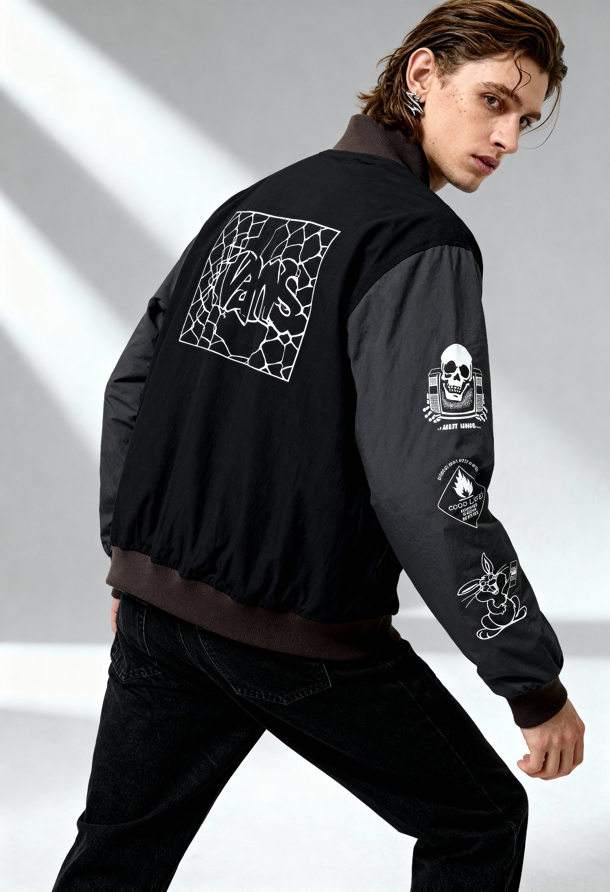 Man wearing Vans VN000JY1KOU1 black bomber jacket showing sleeve graphics and back artwork in studio light.