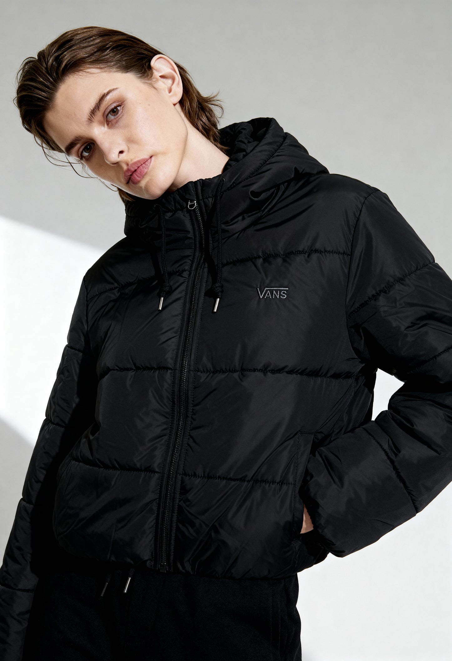 Side angled view of woman wearing Vans VN0A4B8MBLK1 black hooded puffer jacket.