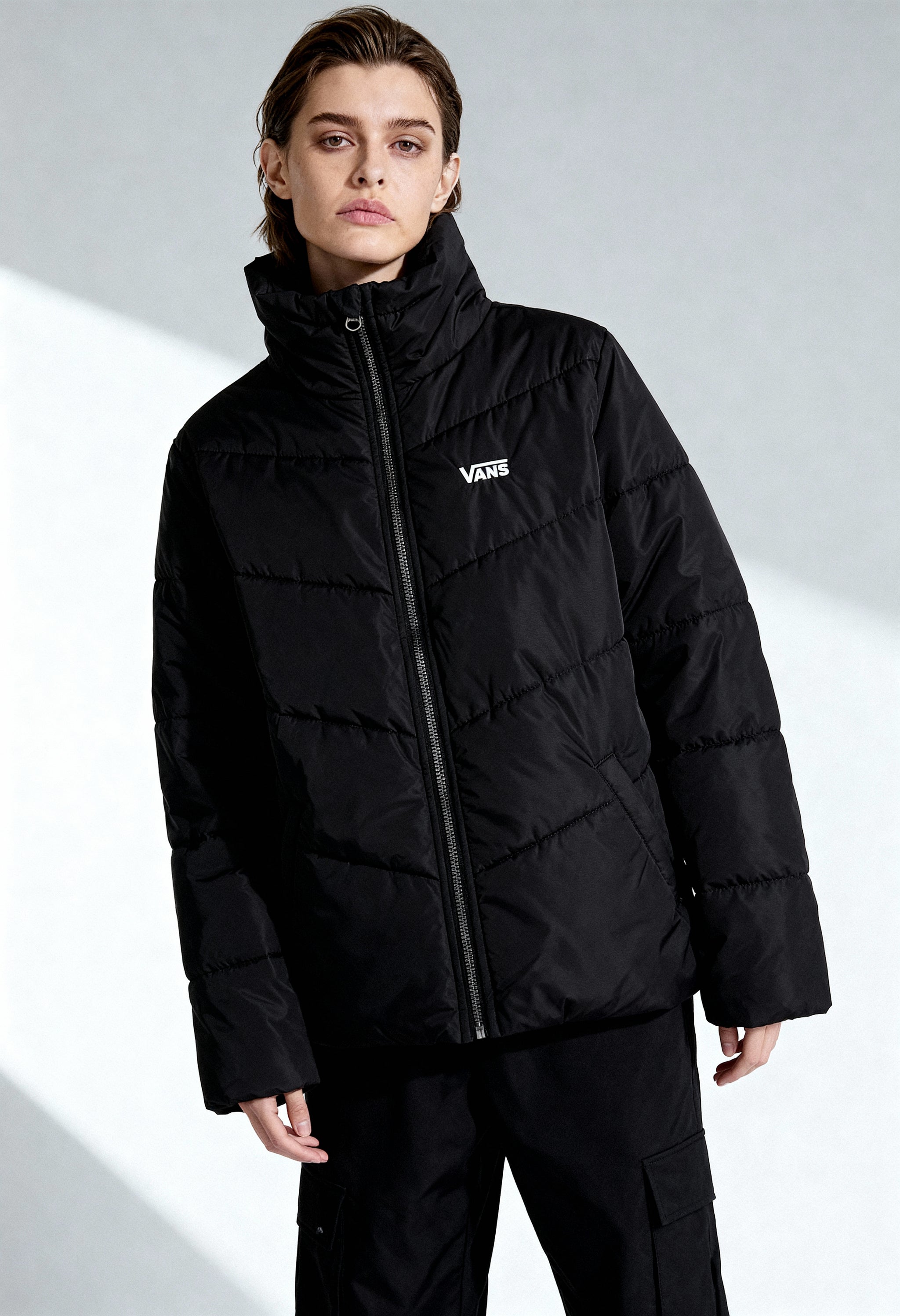 Full-body view of woman wearing Vans VN0A7YK5BLK1 black bomber jacket with zip fastening and long sleeves.