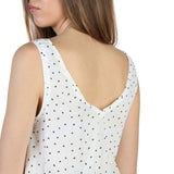 White sleeveless top with black polka dots worn by a person on a white background
