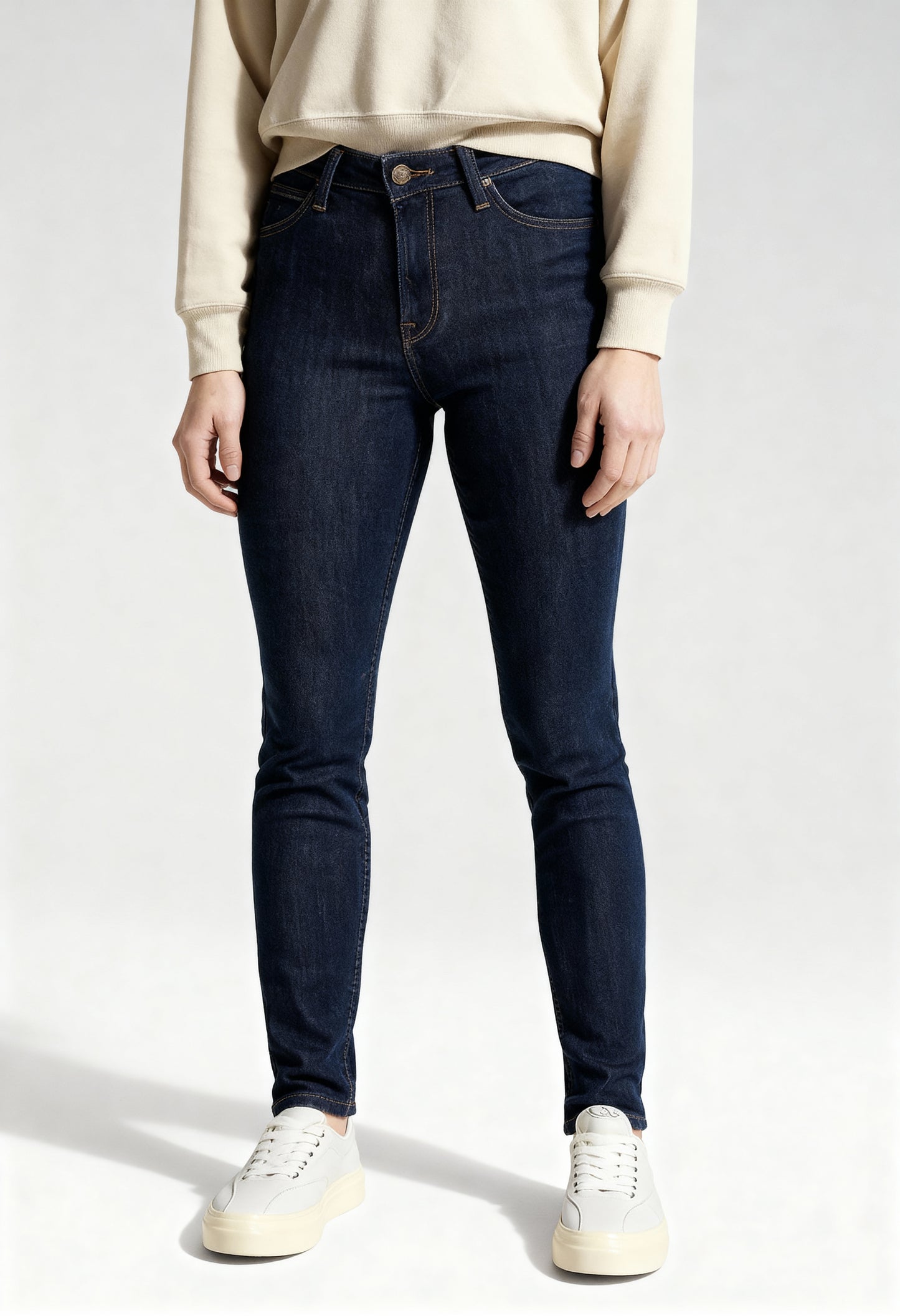 Front view of a woman wearing dark blue Lee L626MDNX skinny jeans on a light background.