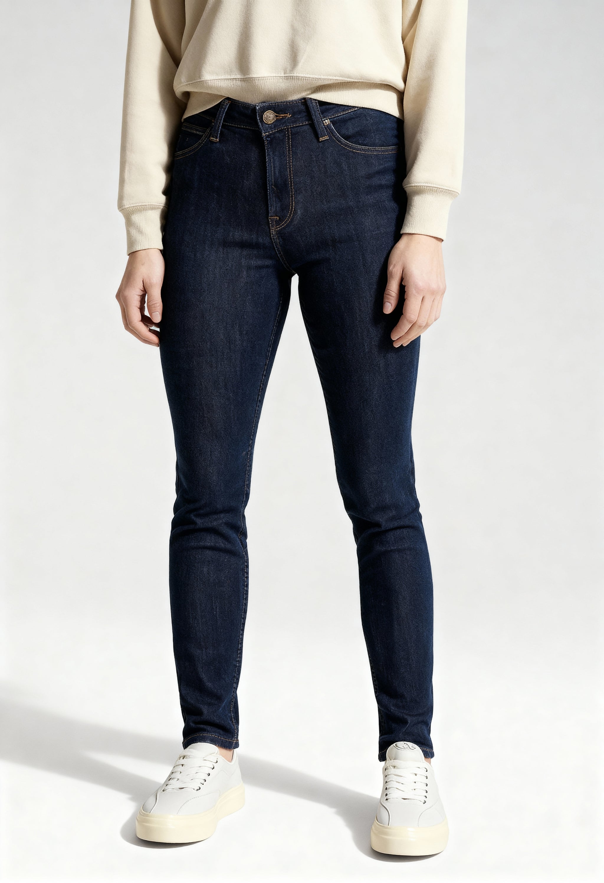Front view of a woman wearing dark blue Lee L626MDNX skinny jeans on a light background.