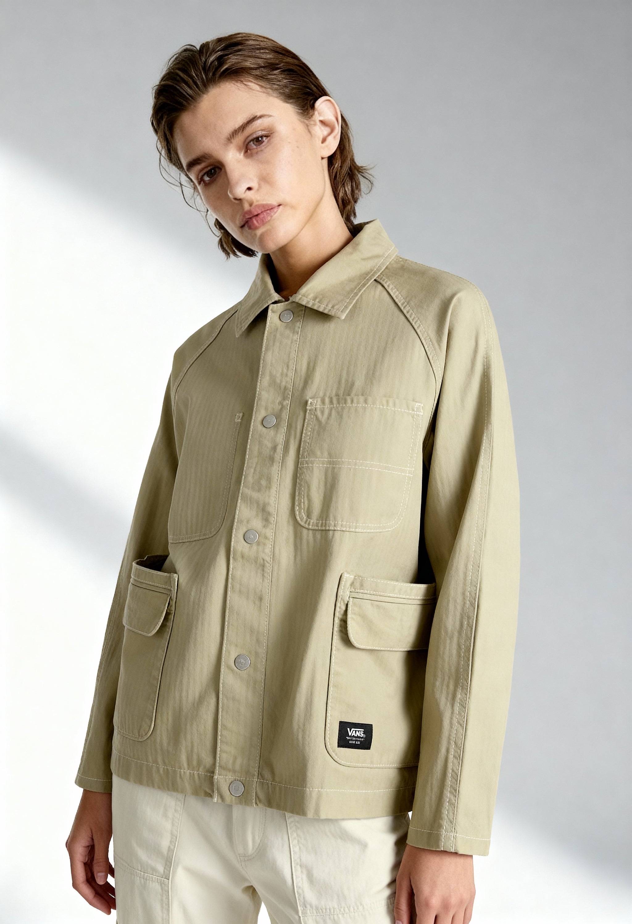 Front angled view of a woman wearing the beige Vans VN000HJRD3Z1 jacket on a light background.